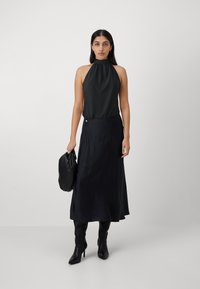 Crna satenska halter top u kombinaciji s crnom satenskom suknjom s bočnim prorezom i minimalističkim detaljima. Dodaci uključuju crnu torbicu.