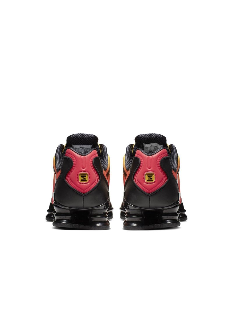 Baskets noires de sport avec des accents roses et jaunes, dotées d'un talon structuré et d'une tige en mesh texturé, conçues pour le soutien et le confort.