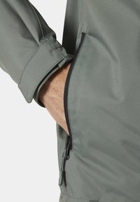 Lichte groene jas met een gladde textuur, voorzien van een ritszak en verstelbare manchetten voor een veilige pasvorm.