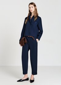 Camicia blu navy con taschino, abbinata a pantaloni a sigaretta coordinati e ballerine nere. Cintura marrone con design intrecciato.