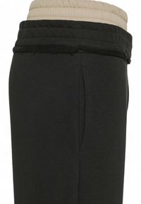 Schwarze Jogginghose mit beiger elastischer Taille, glatter Textur, Seitentaschen und ausgefranstem Saumdetail.