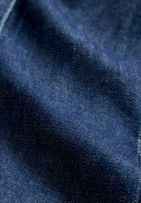 Gros plan sur un tissu denim bleu foncé montrant la texture et le motif de tissage avec des plis doux et des reflets de lumière.