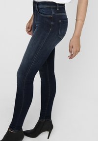 Jeans ajustados en denim oscuro con una textura suave y un ligero desgastado. Presentan costuras decorativas, diseño de cinco bolsillos y una cintura alta.