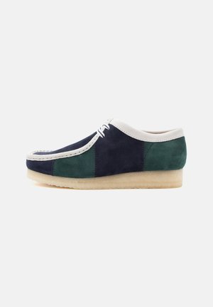 Chaussure décontractée pour homme en daim bicolore avec panneaux bleu marine, vert et blanc, lacets blancs et semelle crêpe beige, vue de profil sur fond blanc.