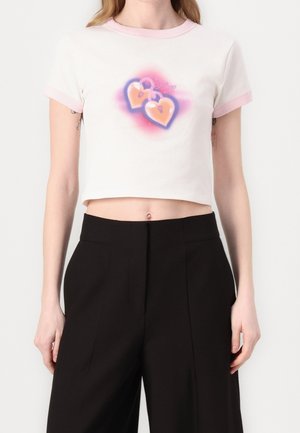 Camiseta blanca corta con cuello y borde de las mangas en color rosa, que presenta un gráfico de dos corazones de dibujos animados con candados, rodeados de un degradado rosa.