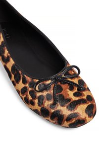 Zapato plano de estampado de leopardo con un acabado texturizado similar al de la piel, interior negro y un detalle de lazo negro en la punta. Forma redonda.
