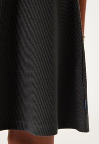 Schwarzes, geripptes Strickkleid mit strukturierter Oberfläche. Es hat einen geraden Saum und ein kleines Markenschild an der Seite.