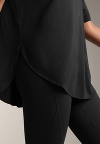 Mustapaita, jossa on kaareva helma ja lyhyet hihat, yhdistetty mustiin leggingseihin, joissa on saumurideet. Sujuva tekstuuri, minimalistinen muotoilu.