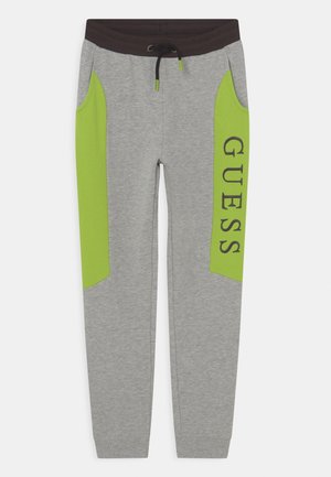 Pantalon de survêtement gris avec panneaux latéraux verts citron, ceinture élastique noire avec cordon de serrage, et texte "GUESS" en caractères gras sur le panneau de la jambe droite.