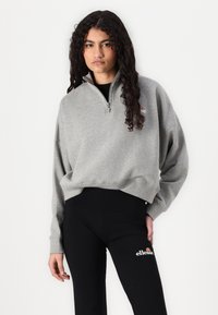 Felpa grigio chiaro, cropped, con colletto a metà zip, polsini a coste e logo ricamato sul petto, abbinata a leggings neri con logo.