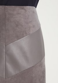 Grauer Rock mit einem Chevron-Muster, das auf der Oberseite mit Wildledertextur und glatten Lederelementen versehen ist. Nahtdetails betonen die Struktur.
