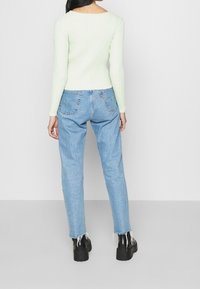 Ljusgrön ribbad tröja med långa ärmar, kombinerad med ljusblå jeans med fransar och svarta platåstövlar.