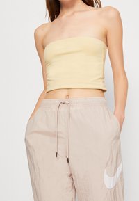Yellow strapless top made of stretchy fabric, paired with light beige, loose-fitting track pants featuring a white Nike logo.