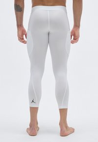 Κολάν συμπίεσης σε λευκό με ματ φινίρισμα, που διαθέτει μαύρο λογότυπο κοντά στον αστράγαλο, απαλή υφή και εφαρμοστή σχεδίαση.