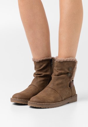 Stivali alla caviglia marroni realizzati in morbida eco-pelle, con un polsino in pelliccia sintetica, cerniera laterale e due bottoni decorativi sul lato esterno.