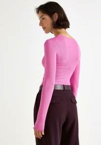Tætsiddende langærmet top i klart pink ribbet stof. Stylet med høj talje mørke burgunder bukser og et slankt sort bælte med knapdetaljer.
