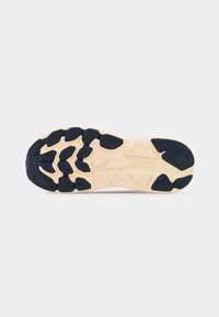 Σόλα αθλητικού παπουτσιού με μπεζ βάση και μαύρες λαστιχένιες επιφάνειες κράτησης, με υφή για πρόσφυση, με ανάγλυφο το λογότυπο της μάρκας στην περιοχή της μέσης του ποδιού.