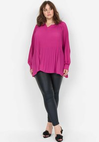 Fuchsiová plisovaná blouse s dlouhými rukávy a výstřihem do V, spárovaná s černými legínami z faux kůže a černými sandály zdobenými květinami.