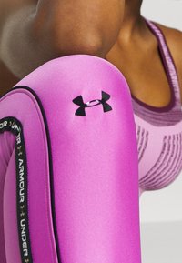 Rosa leggings av mjukt, stretchigt material har en svart logotypdetalj och en kontrasterande svart midja med text.