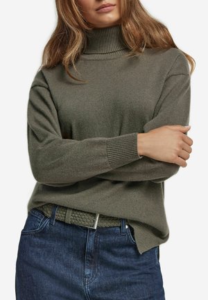 Maglione a collo alto verde oliva in tessuto morbido con polsini a coste, abbinato a jeans blu scuro e una cintura intrecciata coordinata.