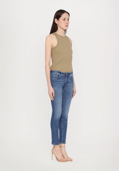 Top sin mangas en color caqui combinado con jeans ajustados azules y tacones nude de tiras. El conjunto presenta un diseño ajustado con una textura suave.