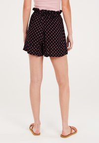 Pantaloni neri con una vita arricciata, caratterizzati da un motivo a diamante rosa. Vestibilità ampia e lunghezza sopra il ginocchio. Sandali marroni visibili.