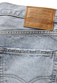Lichtblauwe denim met een vervaagd textuur, met een bruine leren merkembleem op de tailleband en gouden stikdetails.