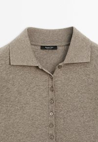 Polo beige en maille côtelée avec col et six boutons marron, étiqueté Massimo Dutti, fabriqué en Chine.