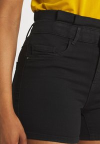 Shorts de mezclilla negra con una cintura alta, que cuentan con pasadores para cinturón, bolsillos delanteros y una tela de textura suave.