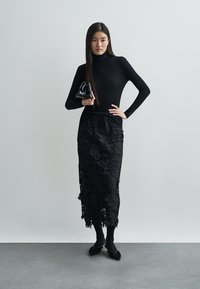 Črna rebrasta majica z visokim ovratnikom, združena s črno cvetlično čipkasto krilo, dopolnjena s črnimi balerinkami in majhno črno torbico.