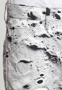 Svartvita jeans med ett tryck som föreställer månens yta, med synlig sömnad, fickor och metalldetaljer. Hållbar tygkvalitet.