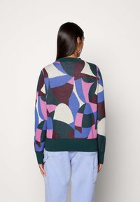 Värikäs neulepaita, jossa on geometrisia kuvioita vaaleanpunaisessa, sinisessä, vihreässä ja kermassa. Ominaisuuksiin kuuluu pyöreä kaulus sekä ribbireunat ja hihat.