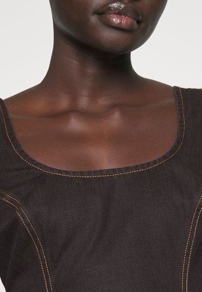 Top en denim noir avec un large col, souligné par des coutures orange. Présente une texture lisse et une coupe ajustée, mettant en valeur la zone des épaules.