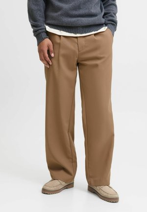 Relaxed-fit brown trousers made of smooth fabric, featuring a flat front, creases down the legs, and side pockets. Paired with beige shoes.