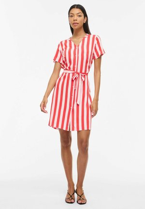 Woman wearing knee-length, short-sleeve dress with red and white vertical stripes and front buttons, tied waist belt, and black sandals.