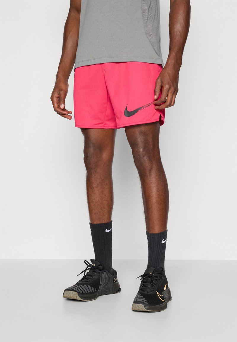 Rózsaszín Nike sort, elasztikus derékrésszel, fekete Nike logóval, fekete sportcipővel és sötétszürke zoknival párosítva. Fent szürke sportpóló.