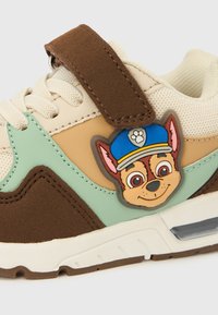 Baskets pour enfants avec des panneaux beige, marron et menthe, ornées d'un badge personnage de Pat' Patrouille et d'une lanière Velcro marron.