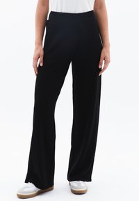 Pantaloni neri a gamba larga realizzati in tessuto morbido, con una cintura elasticizzata. Abbinati a una camicia bianca e scarpe sportive. Texture liscia, senza motivi.