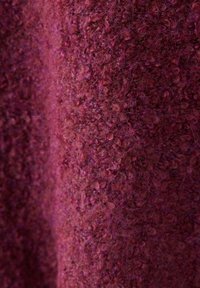 Gros plan d’un tissu doux à texture bouclée dans des tons rouge foncé et violet, montrant les fibres détaillées et les fils en boucle.