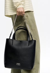 Czarna skórzana torebka typu tote z srebrnymi łańcuszkowymi rączkami i wytłoczonym logo, charakteryzująca się miękką teksturą i minimalistycznym wzornictwem.