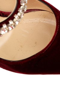 Gros plan d'une chaussure à talon haut en velours bordeaux avec une semelle intérieure beige et une bride de cheville ornée de cristaux.