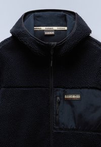 Fleece jacket in dark navy with a textured exterior, full zipper, high collar, and a zippered pocket featuring a branded patch.
