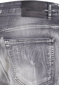 Jeans in denim sbiadito con una finitura grigio chiaro e strappata. Presentano una toppa in pelle nera con testo sulla vita e tasche posteriori standard.