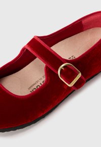 Rød fløyels Mary Jane-sko med gullspenne og beige såle, flat svart såle, Birkenstock-merke på spennen.