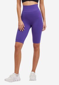 Paarse high-waisted fietshorts met een textuurpatroon, tot halverwege de dij, en een getailleerd ontwerp. Gecombineerd met witte sportschoenen.