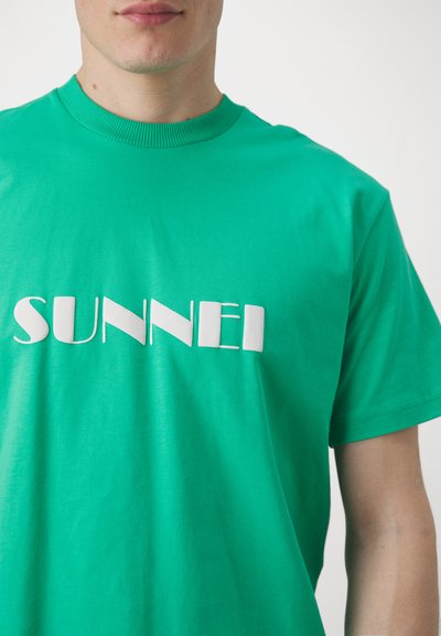 Grønn bomulls t-skjorte med rund hals, med et hvitt trykt logo "SUNNEI" i varierende tykkelse. Myk tekstur, avslappet passform.