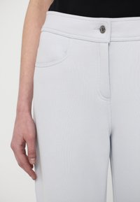 Light blue pants made of textured fabric, featuring a front button closure, side pockets, and a fitted design at the waist and hips.