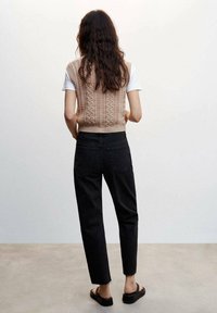 Gilet en tricot beige avec un motif en relief, porté sur un t-shirt blanc, associé à un jean noir taille haute à coupe droite et des sandales noires.