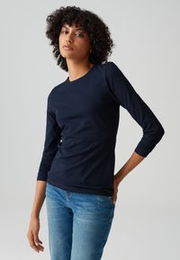T-shirt in cotone a maniche lunghe di colore blu navy con scollo a girocollo e vestibilità slim, abbinato a jeans in denim blu chiaro. Texture morbida, design minimal.