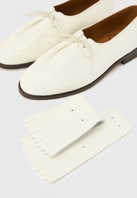 Chaussures en cuir blanc à finition texturée, dotées d'un bout arrondi et de lacets. Accompagnées de franges en cuir assorties.
